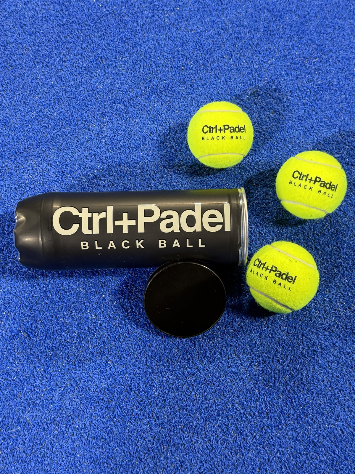 Ctrl+Padel Black Ball tube with three balls on a blue padel court
